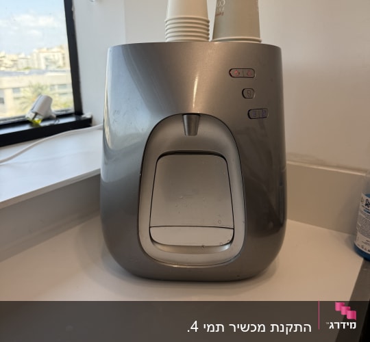 מכונת מים עם כוסות חד פעמיות על השיש